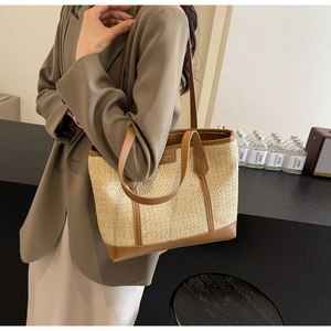 Detailed view of handwoven straw tote bag featuring brown leather trim on a model