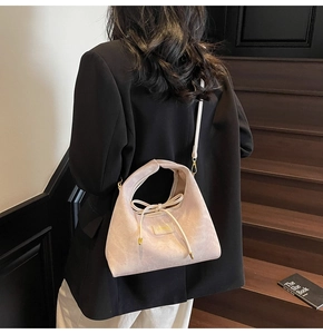 Detail of beige corduroy dumpling bag with bow strap on a model against dark stairs