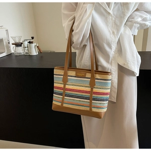 Detail view of multicolored striped straw tote bag with brown leather handles and base