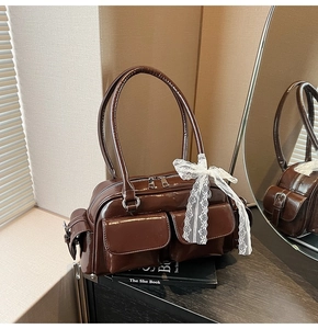 Detail view of glossy brown Boston bag with lace bow and silver hardware accents