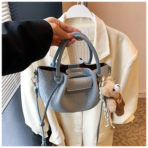 Détail du sac seau plissé bleu clair avec breloque ours en peluche marron et bandoulière