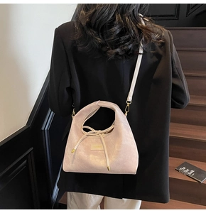 Detail of light beige crossbody bag with decorative bow and gold metal logo plaque