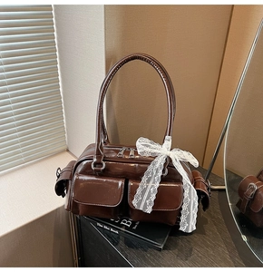 Detail of a coffee brown glossy Boston bag featuring front pockets and a white lace bow accent