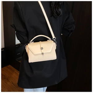 Détail du sac beige avec cuir lisse, texture tissée et boucle métallique ronde élégante