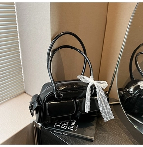 Detail of black patent leather Boston bag featuring white lace bows and side buckle pockets
