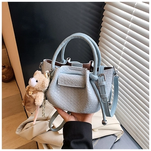 Détail d'un sac seau plissé bleu clair avec texture tressée et un petit pendentif d'ours