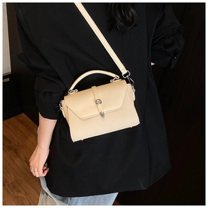 Détail d'un sac bandoulière tissé beige avec fermoir métallique sur un blazer noir