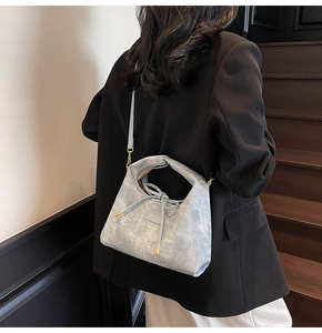 Detail of light gray textured crossbody bag with gold logo plaque and drawstring