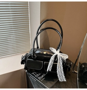 Detail of a black patent leather Boston bag featuring two front pockets and a white lace bow