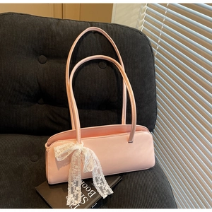 Close-up of pink rectangular baguette bag with a white lace bow on black velvet