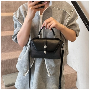 Détail du sac à bandoulière noir avec fermoir rotatif argenté et texture tressée