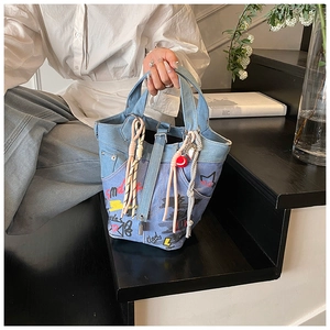 Detail of blue denim bucket bag with colorful graffiti prints and pink knot charms
