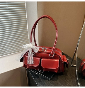 Detailed view of red glossy Boston bag with cargo pockets and a lace bow charm on books