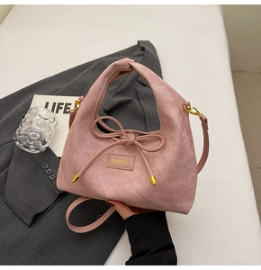 Detail showing pink suede handbag with bow accent and gold hardware on grey background