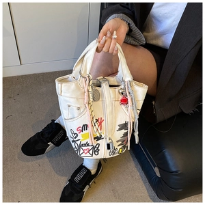 Detail of white canvas bucket bag featuring artistic hand-drawn graffiti and colorful charms