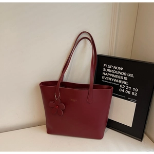 Detail der weinroten PU-Leder-Tote mit Goldlogo und Blumenanhänger-Accessoire