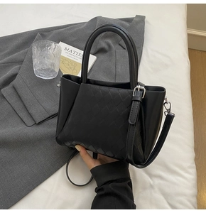 Detail of black leather bucket bag with quilted texture next to art book and blazer