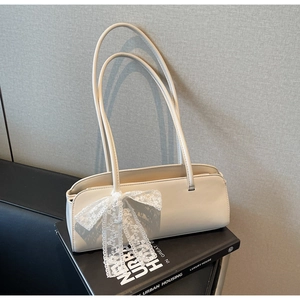 Schicke cremefarbene Leder-Baguette-Tasche mit Spitzenschleife auf minimalistischem Buch
