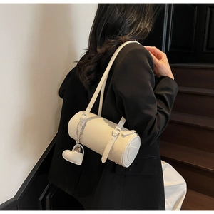 Detail of a minimalist off-white cylinder shoulder bag with a heart charm and silver hardware
