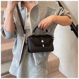 Sac bandoulière noir avec fermoir métallique rond et détails tressés portés par un modèle