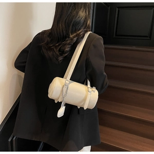 Detail of a creamy white cylindrical pillow bag with silver chain and adjustable strap
