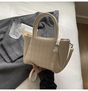 Detail of cream quilted crossbody bucket bag with silver hardware and top handles