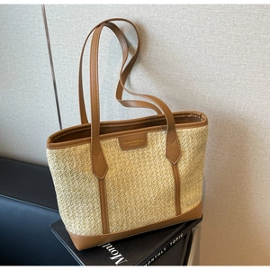 Close-up of beige straw tote with brown leather corners and fashion logo patch