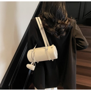 Detail of cream barrel bag with heart charm worn over the shoulder on a black blazer