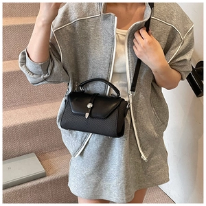 Détail d'un sac à bandoulière noir avec texture diagonale et boucle ronde argentée