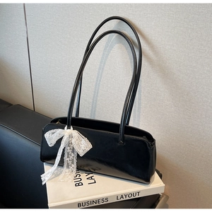 Detail of black leather underarm bag featuring a large white lace bow and sleek finish
