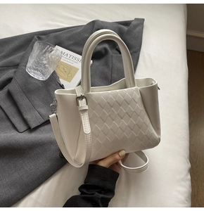 Detail of white quilted handbag showing dual handles and detachable shoulder strap