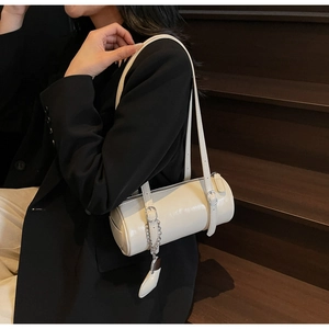 Detail of a creamy white cylindrical shoulder bag with silver chain on model