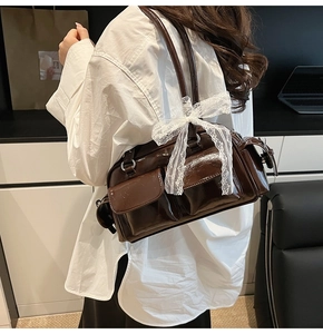 Detail of dark brown glossy Boston bag featuring multi-pocket design and lace bow