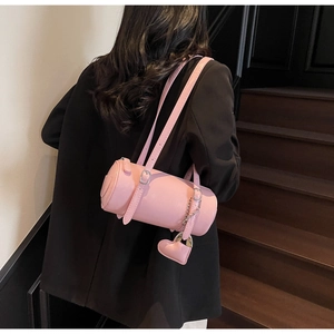 Close-up of pink cylindrical leather shoulder bag with a heart charm on a model