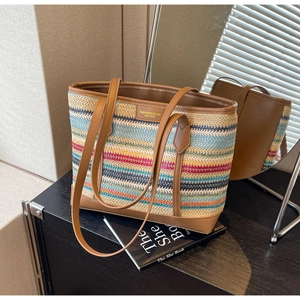 Detail of colorful striped straw tote bag with brown leather handles and brand patch
