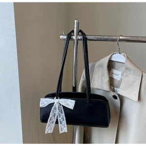 Detail of black shoulder bag featuring a large white lace bow on faux leather finish