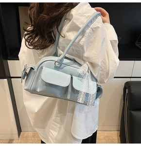 Detail of light blue Boston bag with dual front pockets and white lace ribbon bow decor