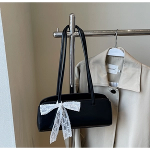 Detail of black glossy shoulder bag with a large white lace bow and dual strap design