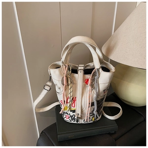 Detailed view of white graffiti bucket bag with woven rope charms on a leather book