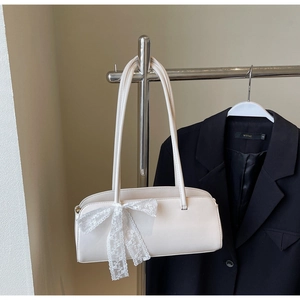Detail of a creamy white shoulder bag featuring a large lace bow on matte leather
