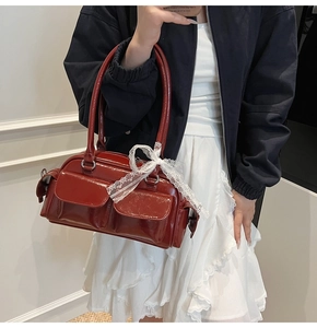 Detail of burgundy glossy Boston bag with front flap pockets and white lace bow accessory