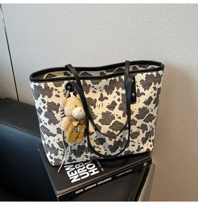 Detail of cow print canvas tote bag with black handles and a cute plush bear charm