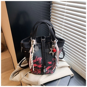 Detail of dark denim bucket bag featuring red graffiti prints and decorative charms