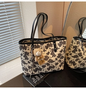 Detail of cow print tote bag with black leather handles and cute plush bear charm decoration