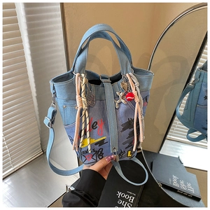 Detail of light blue denim bucket bag with graffiti prints and metal charms on books