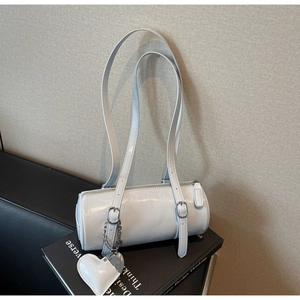 Detail of white barrel bag with heart charm on black book and leather sofa