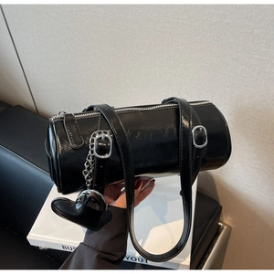 Detail of black glossy patent leather cylinder bag with silver zipper and heart pendant