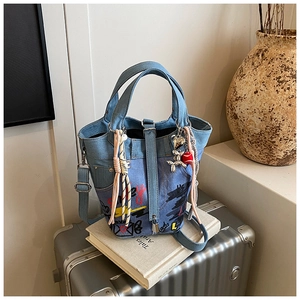Detailed close-up of blue denim bucket bag with colorful graffiti and creative charms