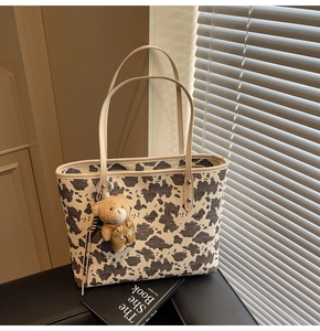 Detail of cow print tote bag with cream leather strap and plush bear charm on black leather