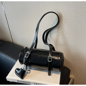 Detail of glossy black cylinder bag with silver buckles and heart-shaped pendant charm